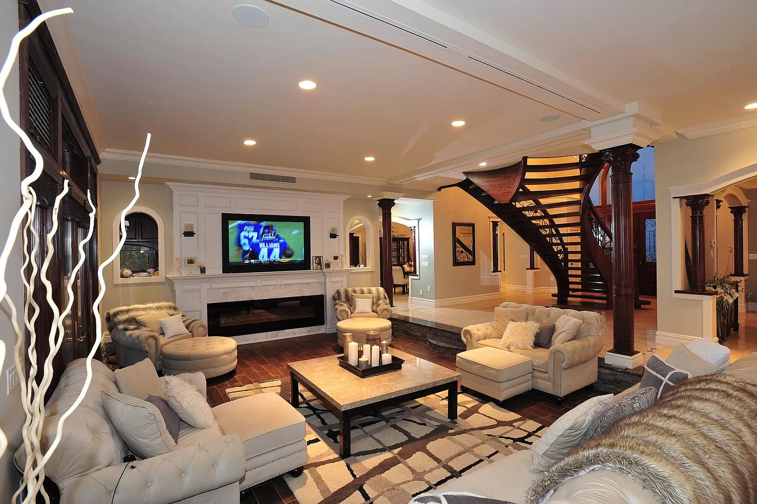 Finished living room with marble fireplace, columns, and curved staircase